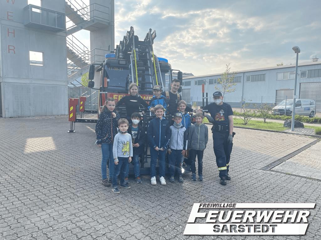 Jugendliche und Ausbilder der Feuerwehr Sarstedt vor einem Drehleiterfahrzeug.